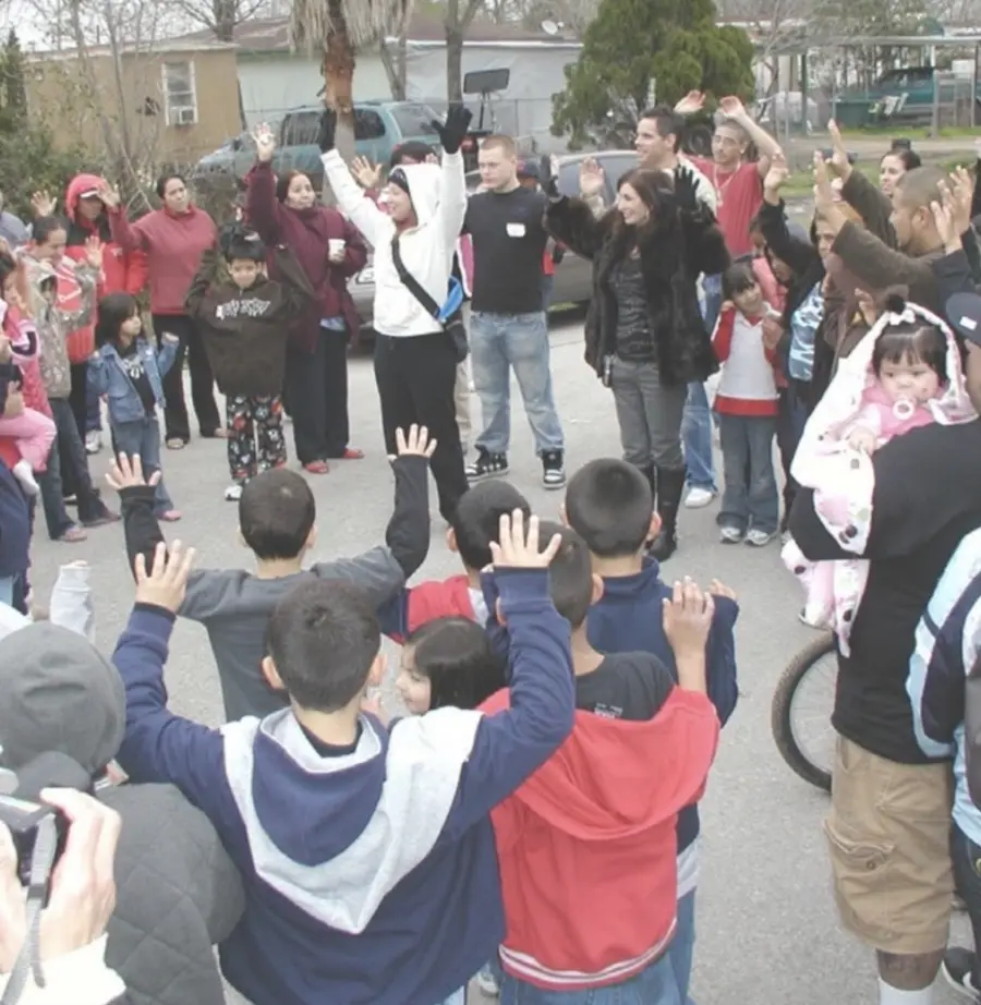 Children and families raising their hands in worship on a street