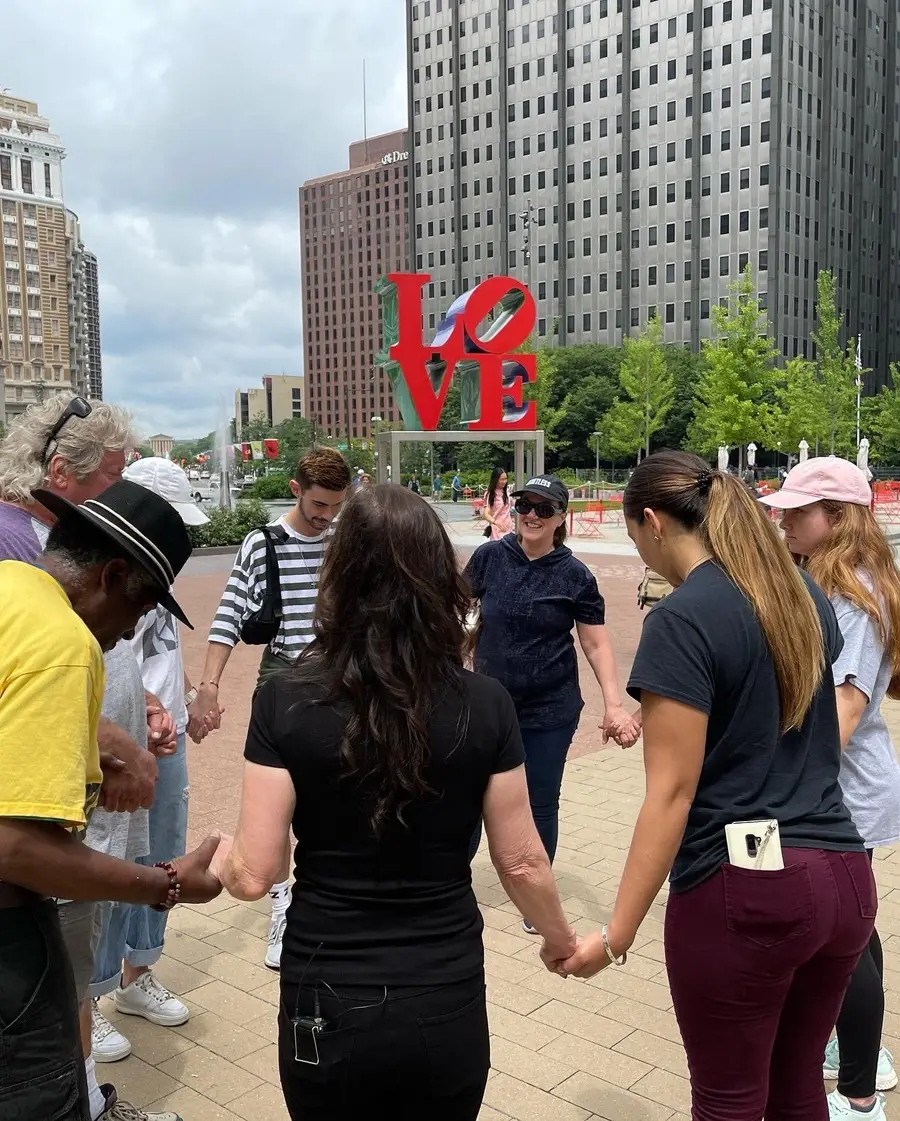 A team holding hands in a prayer circle near the LOVE sculpture
